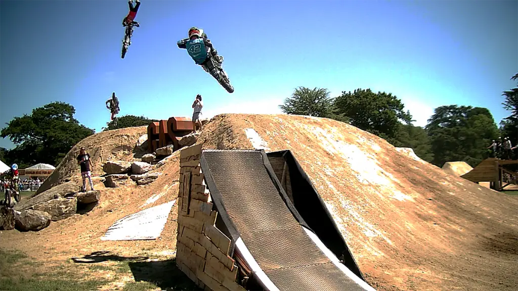 Three arena cross motorcycle stunt riders flying through the air above two presenters